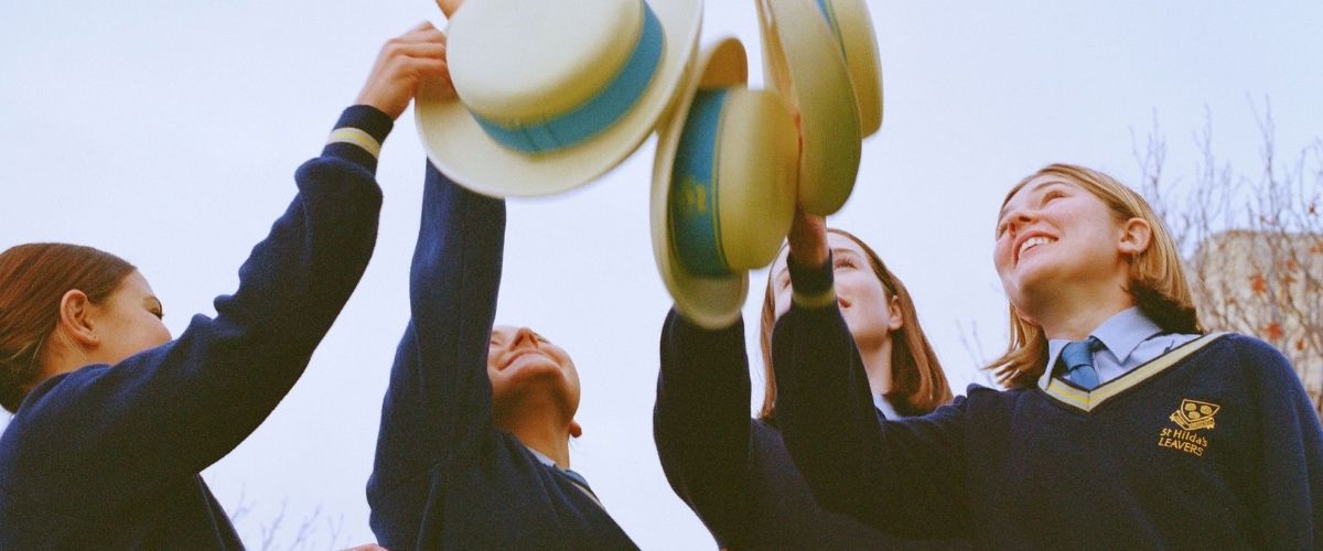 Group of students in uniform raising hats in the air in celebration outdoors under a clear sky.