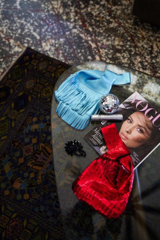 Artist on Show_LetitiaGreen_AfterHours - St Hilda's Anglican School For Girls Blue fringe clutch and red metallic purse rest on a glass coffee table, with a small disco ball, a dark hair clip, and a Vogue magazine nearby.