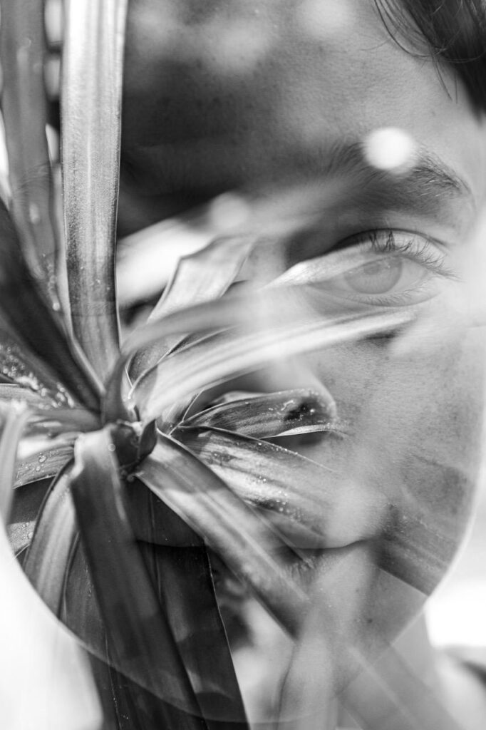 Artist on Show_LetitiaGreen_DoubleExposure - St Hilda's Anglican School For Girls Close-up black-and-white photo of a person’s face partially obscured by tropical leaves in front of them.