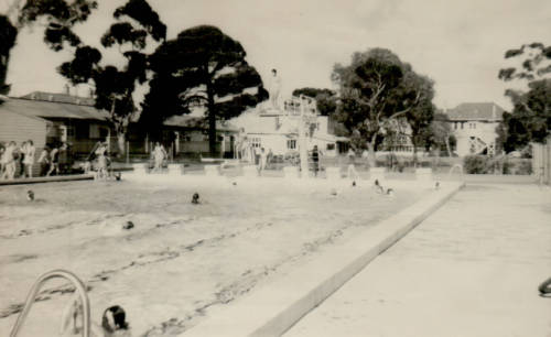 1965 Swimming Pool - St Hilda's Anglican School For Girls Outdoor public swimming pool with diving boards, swimmers in the water and on the deck, trees and buildings in the background.