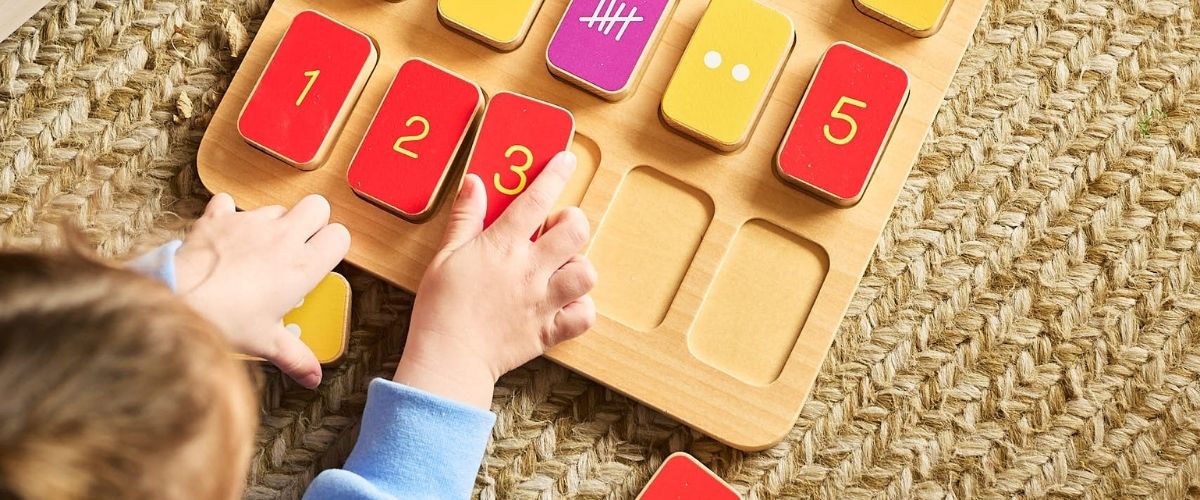 Child's hands place or rearrange red number blocks (1–3) on a wooden counting puzzle atop a woven rug