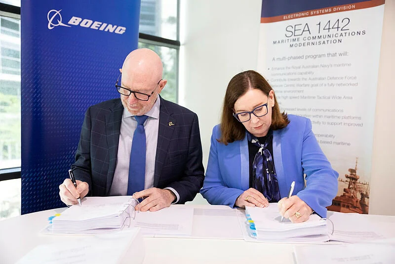 Signing a contract with Boeing - St Hilda's Anglican School For Girls Two professionals in business attire sign documents at a table during a formal signing event, with Boeing branding visible in the background.