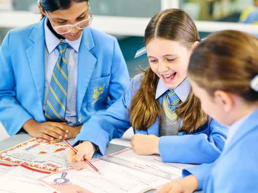 Students in blue uniforms work together on a map or project at a table, guided by a teacher.