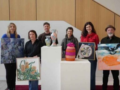 Six people stand behind white display pedestals with colorful artworks and pottery in a gallery setting, posing for a group photo.