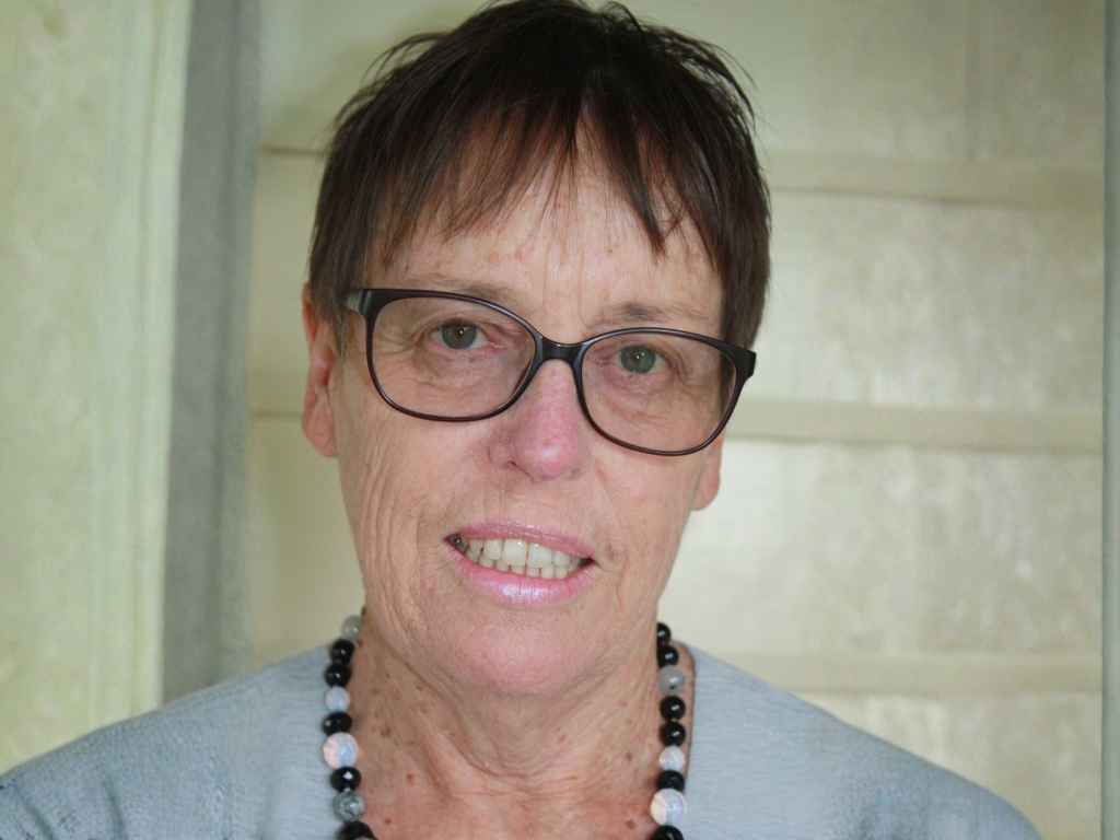 Portrait of a middle-aged woman with short dark hair and rectangular glasses, wearing a beaded necklace.