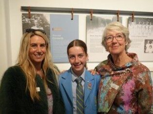 f_2_34489987 - St Hilda's Anglican School For Girls Three smiling people pose indoors; center is a student in a blue blazer and striped tie, flanked by two adults.