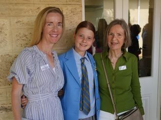 f_2_34490037 - St Hilda's Anglican School For Girls Three women pose outside a stone building, all with name badges; left in a striped dress, center in a blue blazer, right in a green blouse.