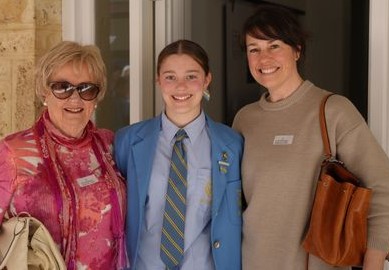 f_2_34490093 - St Hilda's Anglican School For Girls Three women standing in a doorway smiling at the camera: an older woman in a pink patterned jacket with sunglasses, a student in a blue blazer and striped tie, and another woman with a brown purse.