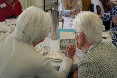 f_2_34547759 - St Hilda's Anglican School For Girls Two elderly women with white hair sit at a dining table, looking at a small photo card together during a meal.