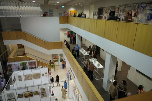 f_2_34611335 - St Hilda's Anglican School For Girls Two-story art gallery or exhibition hall with wooden railings, white walls, and visitors exploring displays on both levels.