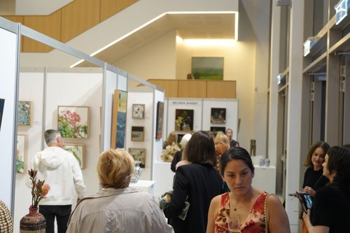 f_2_34611338 - St Hilda's Anglican School For Girls Crowded art gallery with visitors browsing framed paintings in white booth walls.