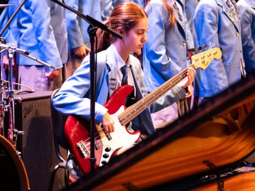 Student performing bass guitar alongside school choir at an independent high school music concert